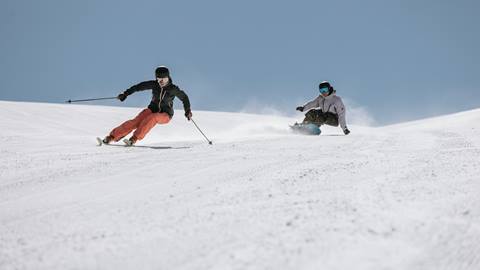 Adults skiing and snowboarding down freshly groomed trails at June Mountain