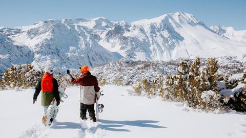 two friends walking in the snow ready to snowboard