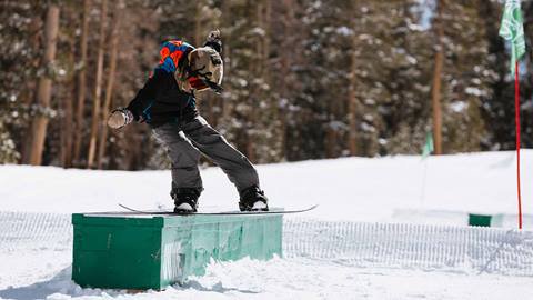 Child snowboarding on a box rail at June Mountain's terrain park
