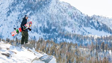 snowboarder standing on a cliff looking over the scenery