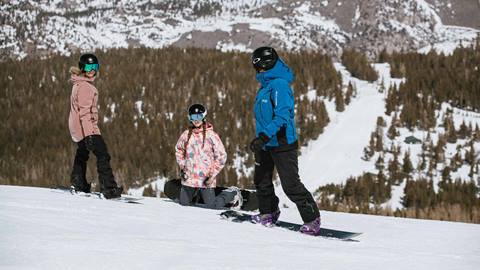 A professional instructor conducting a group snowboard lesson for two students at June Mountain