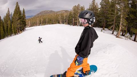 A young snowboarder practicing turns on a wide, sunny trail at June Mountain