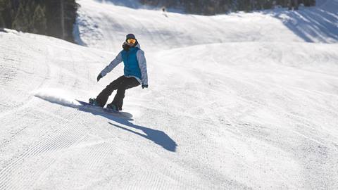 A snowboarder carving on a perfectly groomed run at June Mountain