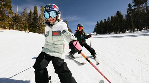 Two young skiers confidently navigating a groomed trail at June Mountain